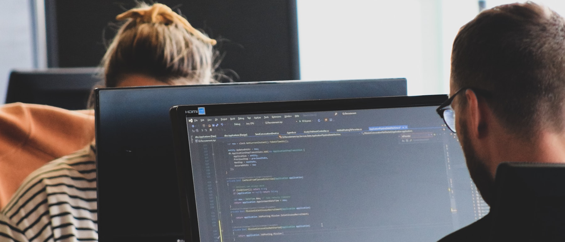 Two developers working side by side at desktop monitors showing code